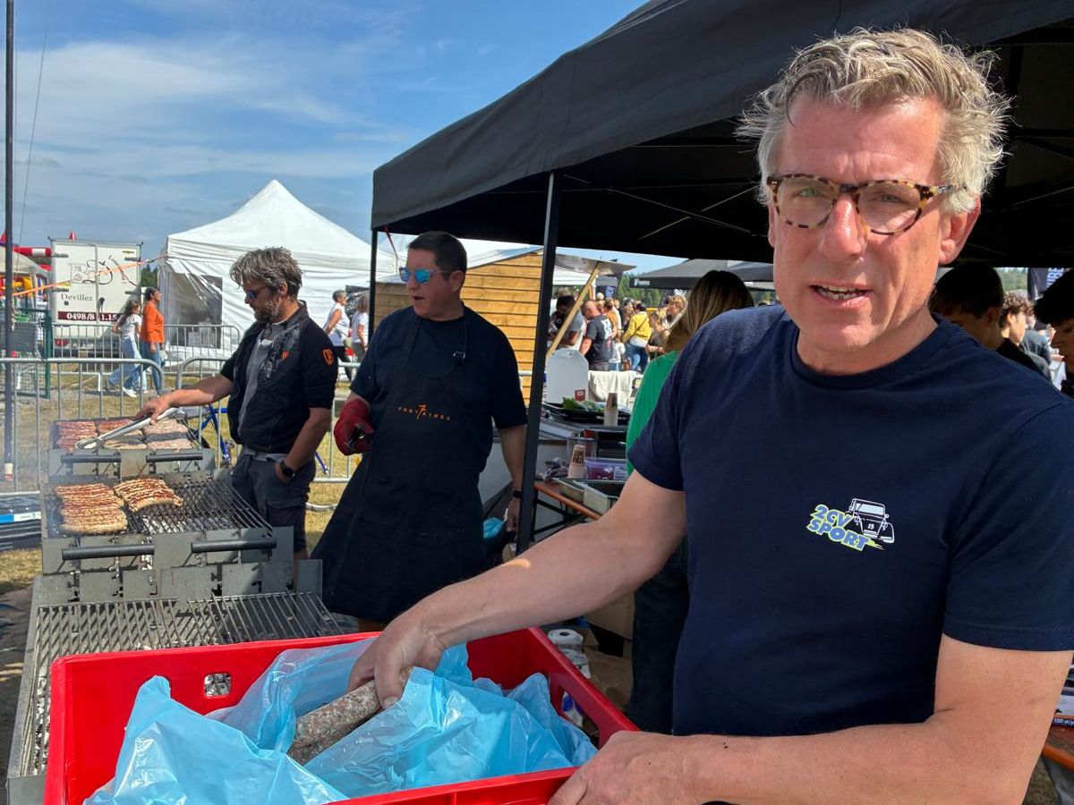 Un membre de l'équipe en t-shirt 2CV Sport apporte une caisse de saucisses