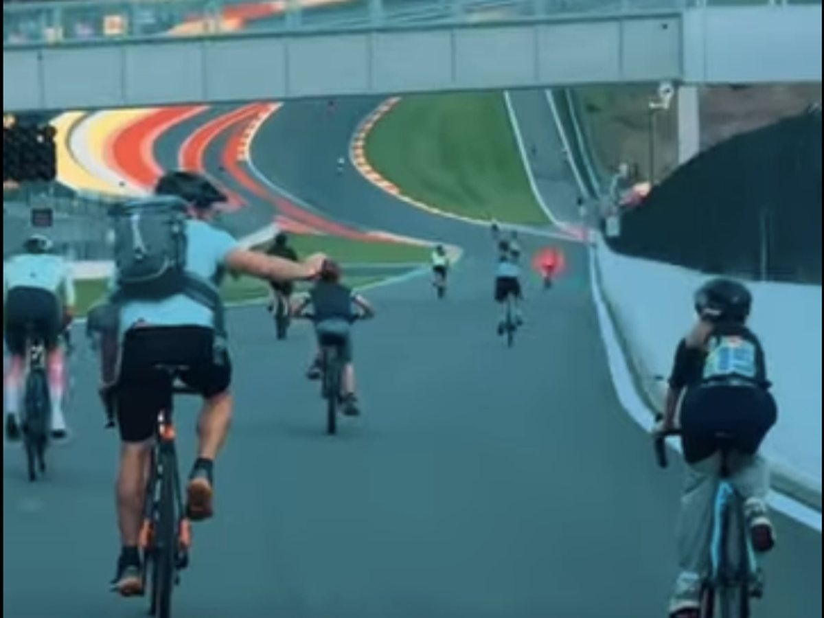 Des cyclistes montent le Raidillon à vélo, sous la passerelle, en direction de l'Eau Rouge